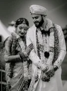 A black-and-white photo of a smiling bride and groom in wedding garlands, the groom in a turban
